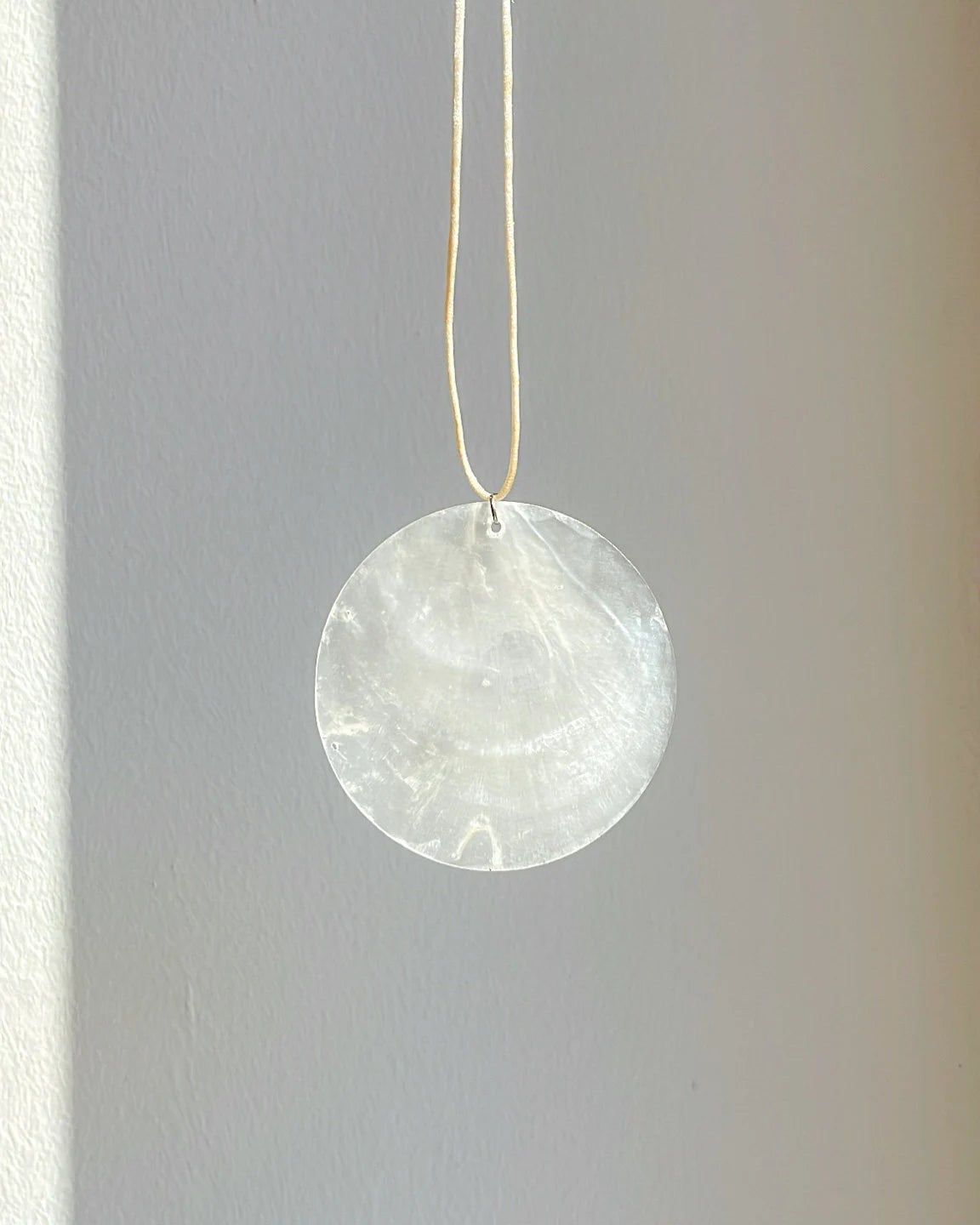 Round white stone pendant hanging on a string against a plain background