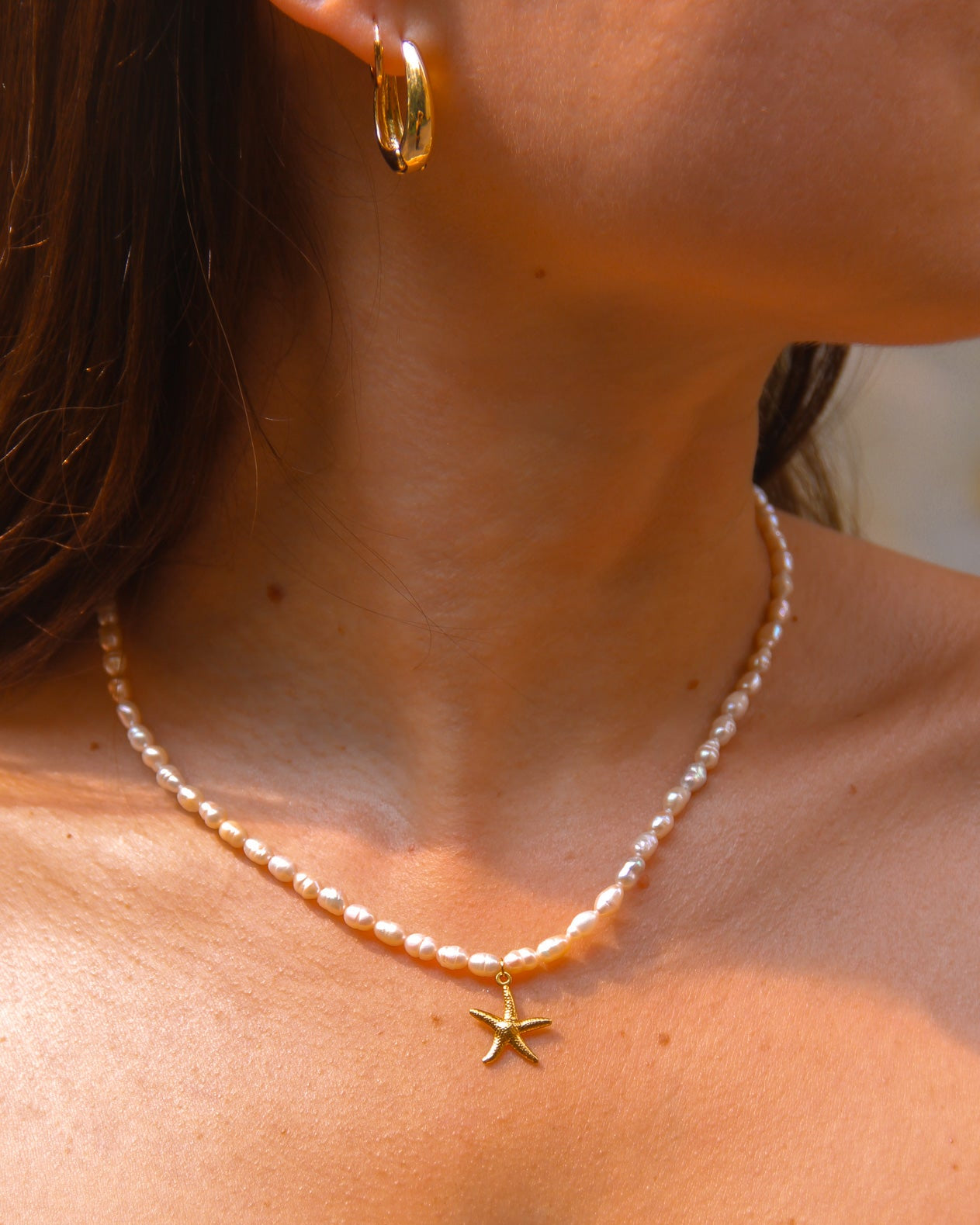 Close-up of a person wearing a pearl necklace with a starfish pendant.